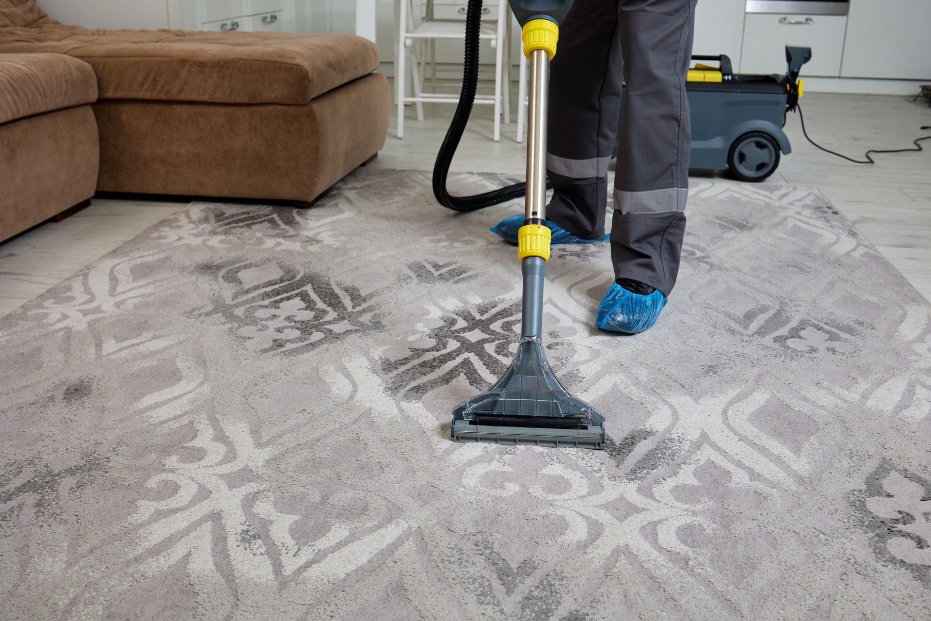 Cleaning agency worker in overalls operates vacuum on living room carpet
